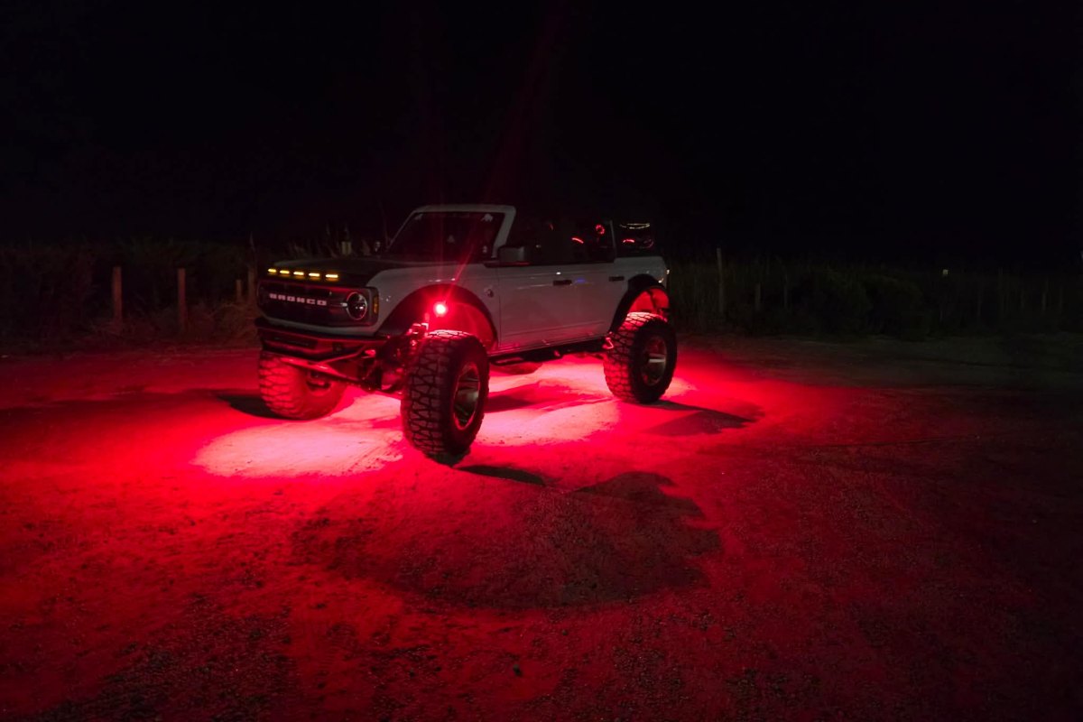 Lifted Ford Bronco illuminated by red Axion rock lights at night.