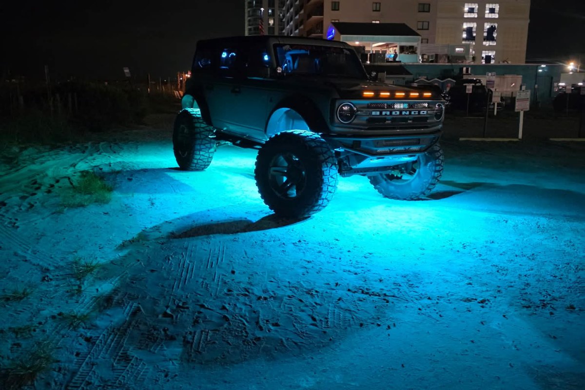 Ford Bronco surrounded by teal Axion underbody and wheel-well lighting at night.