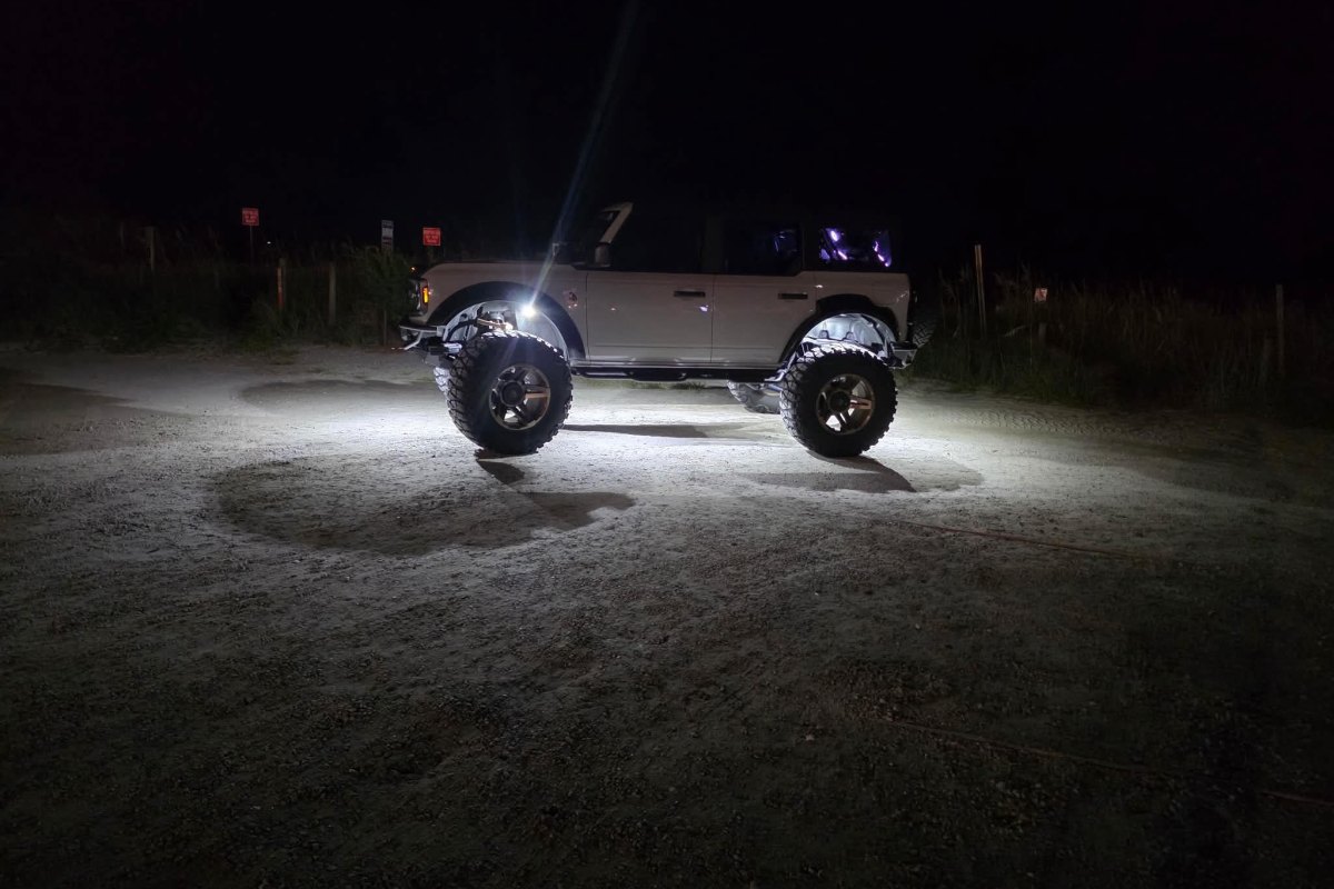 Lifted Ford Bronco illuminated by bright white Axion rock lights at night.