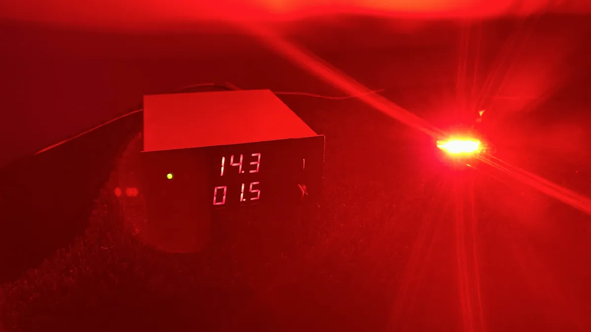 An Axion rock light on the bench firing red, with the supply reading 14.3 volts and 1.5 amps